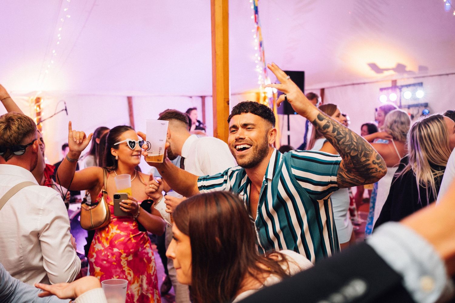 Energetic crowd dancing and celebrating at a lively party with colorful lighting and festive atmosphere.