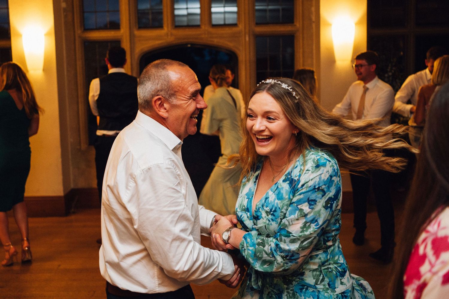 People dancing and celebrating at a wedding reception with warm ambient lighting in the background.