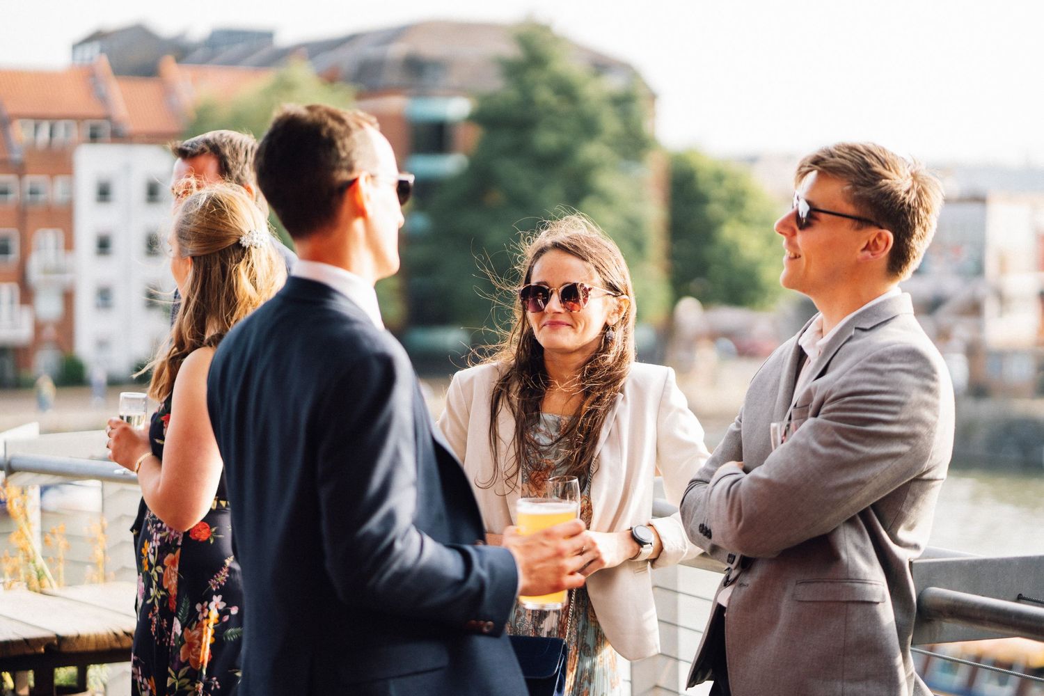 Well-dressed guests enjoying drinks and conversation on an outdoor terrace overlooking a city view.