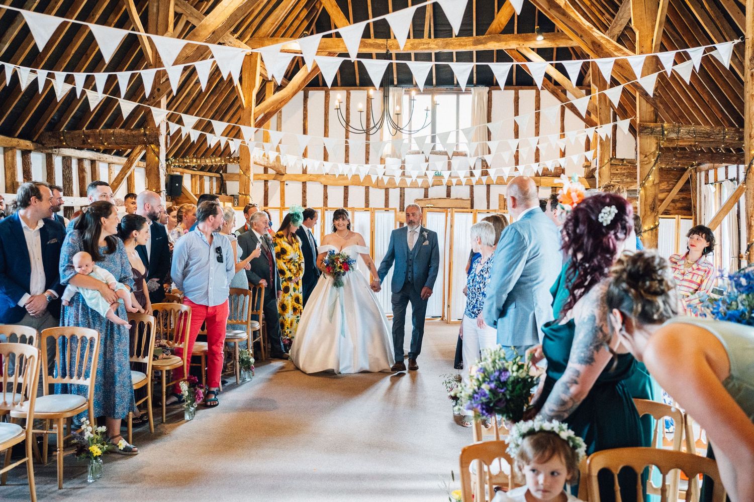 Rustic barn wedding venue interior decorated with white bunting and string lights showing long reception tables.
