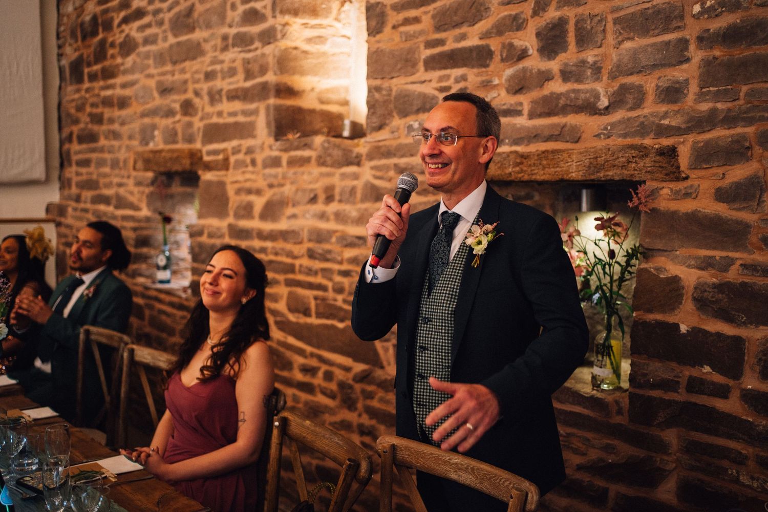 Wedding guests share joyful laughter during reception celebration in rustic stone-walled venue.