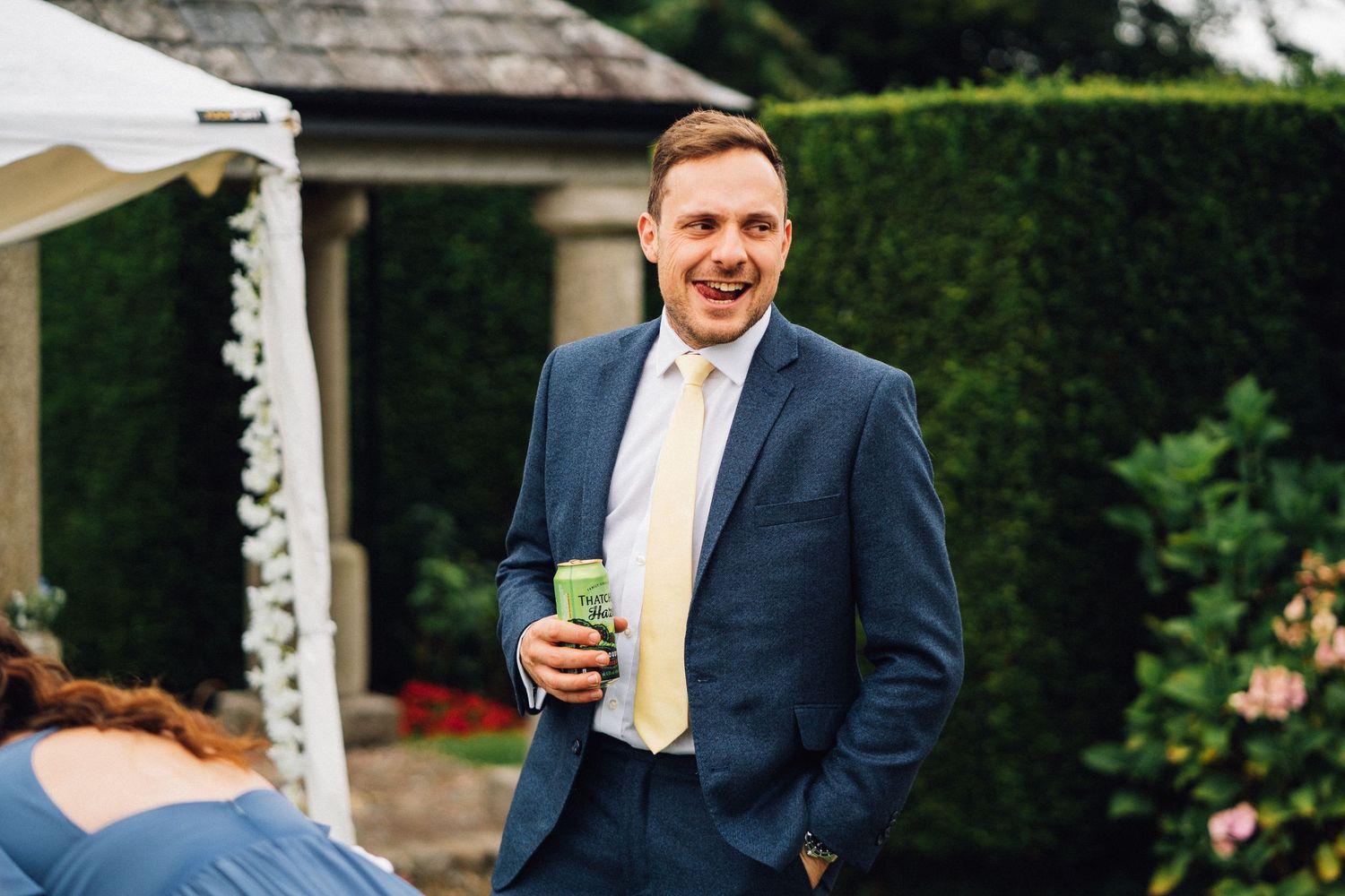 Wedding party members stand outdoors in formal attire against a lush garden backdrop.