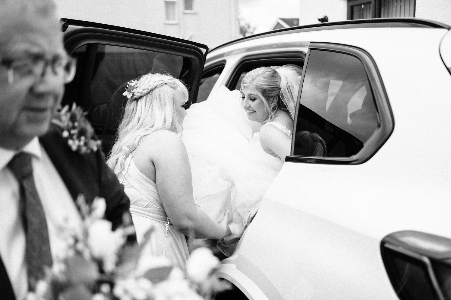 Black and white photo of wedding guests arriving in cars and greeting each other.
