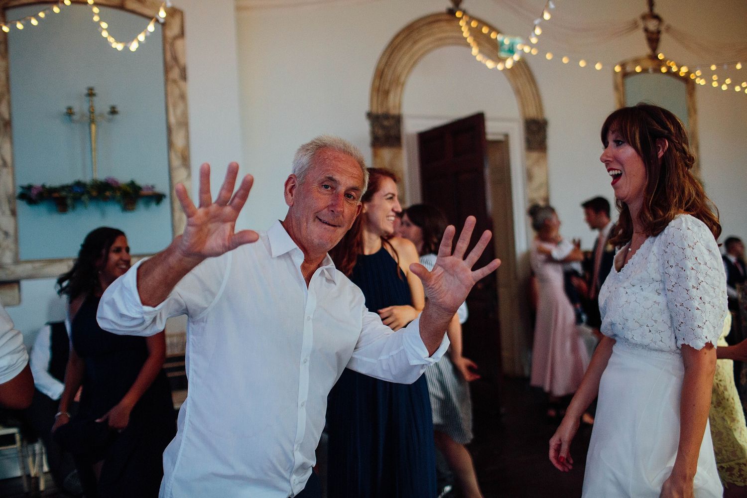 Wedding guests dance and celebrate on an indoor dance floor decorated with string lights.