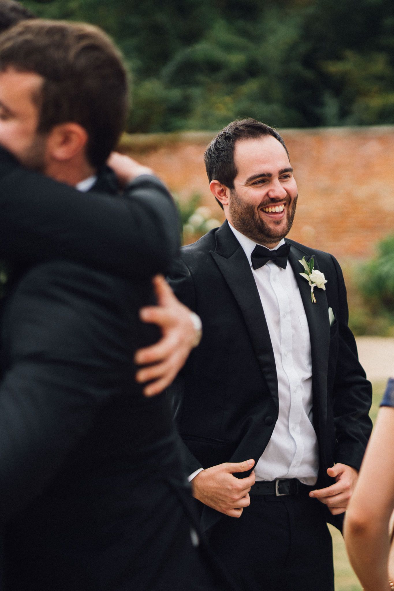 Groomsmen in black tuxedos sharing laughs during outdoor wedding celebrations.