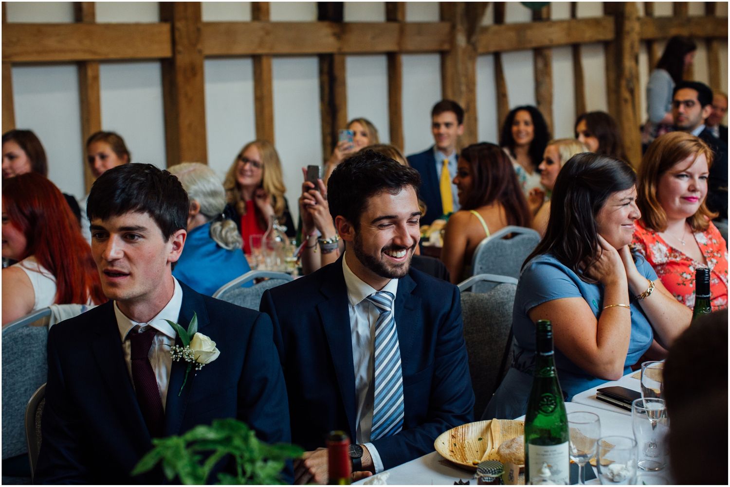 Wedding guests dining and socializing at rustic timber-framed reception venue.