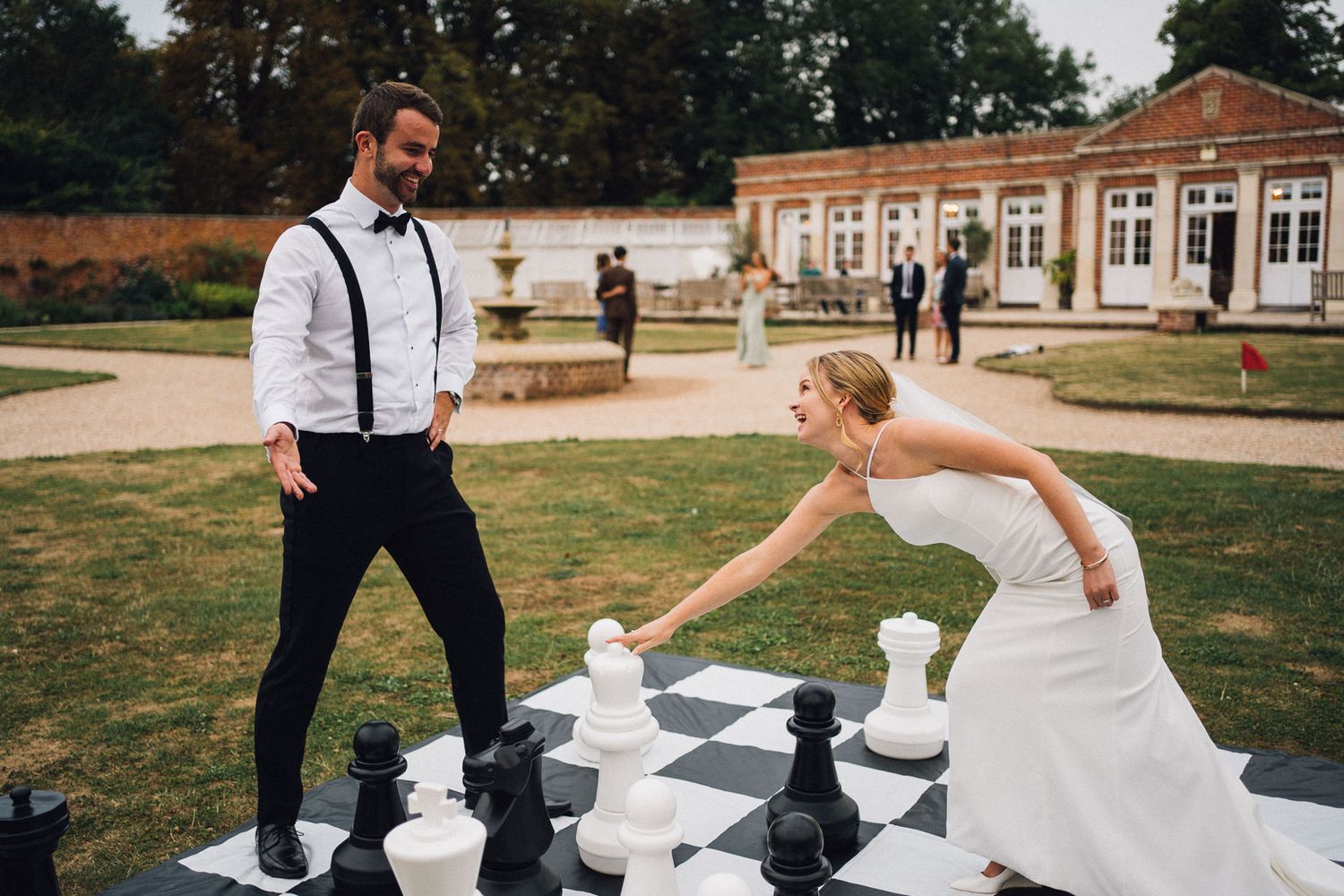 A bride and groom engage in a playful game of giant chess on a sunny day.