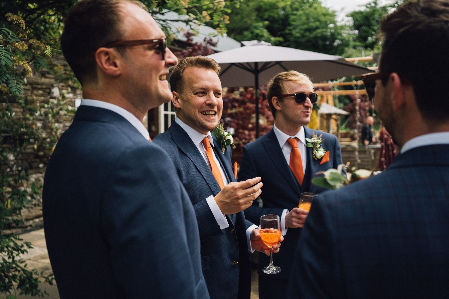 Groomsmen in navy suits socialize during outdoor wedding reception.
