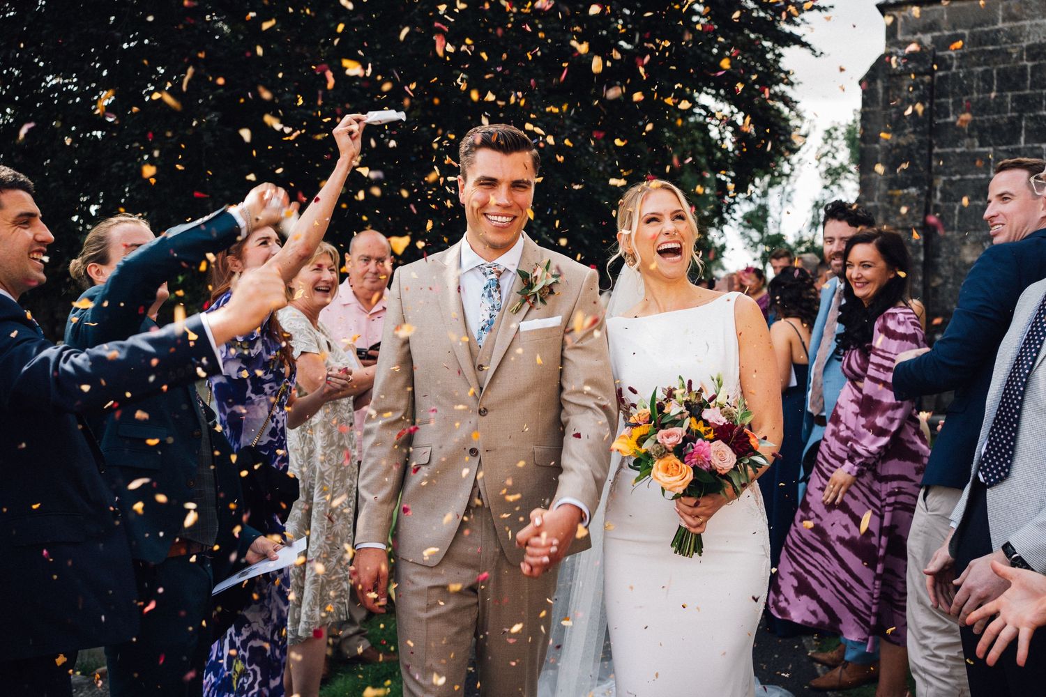 Confetti fills the air as newlyweds celebrate with guests outside church.