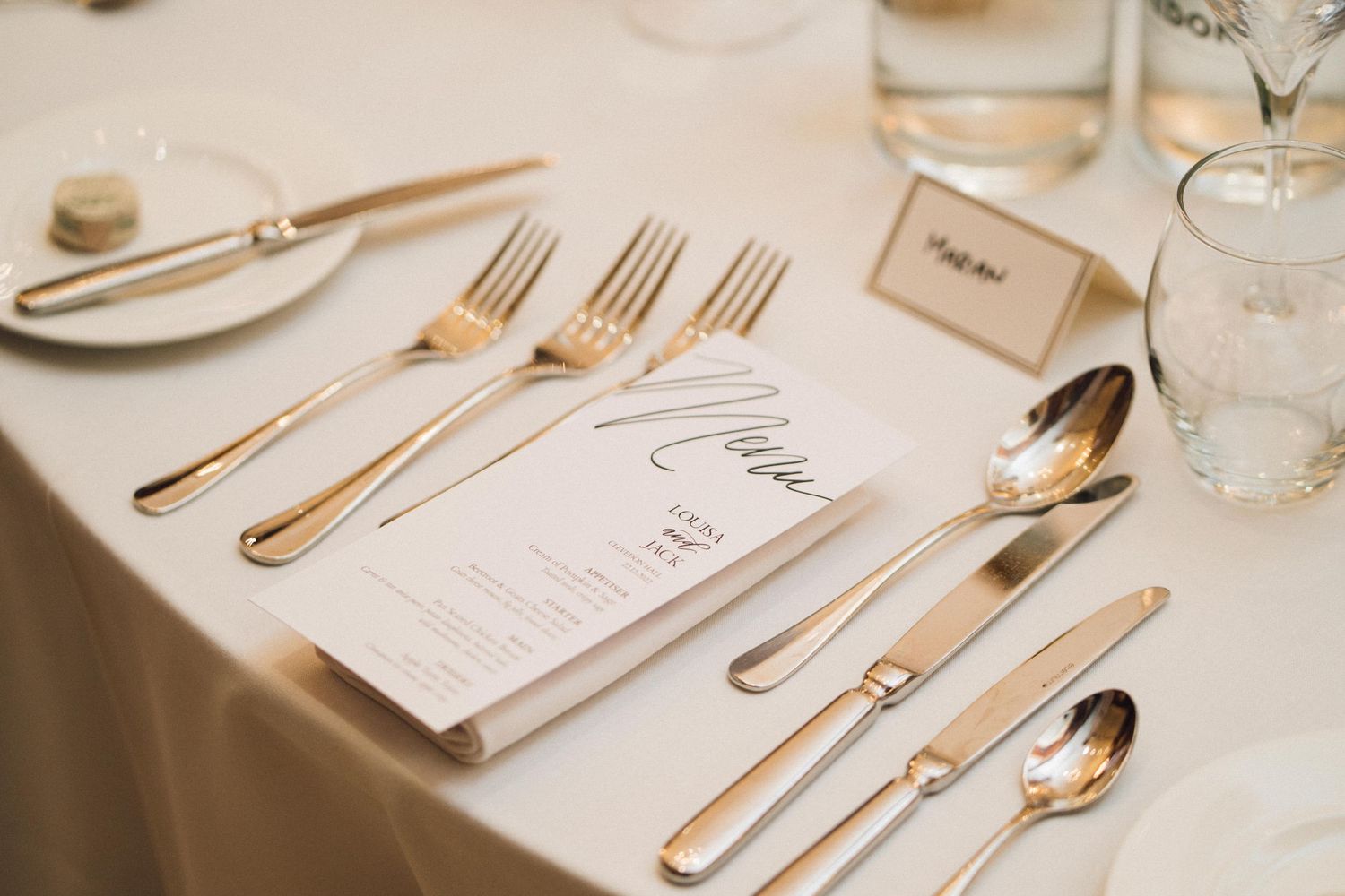 Elegant place settings with gold cutlery and menu cards at a formal wedding reception.