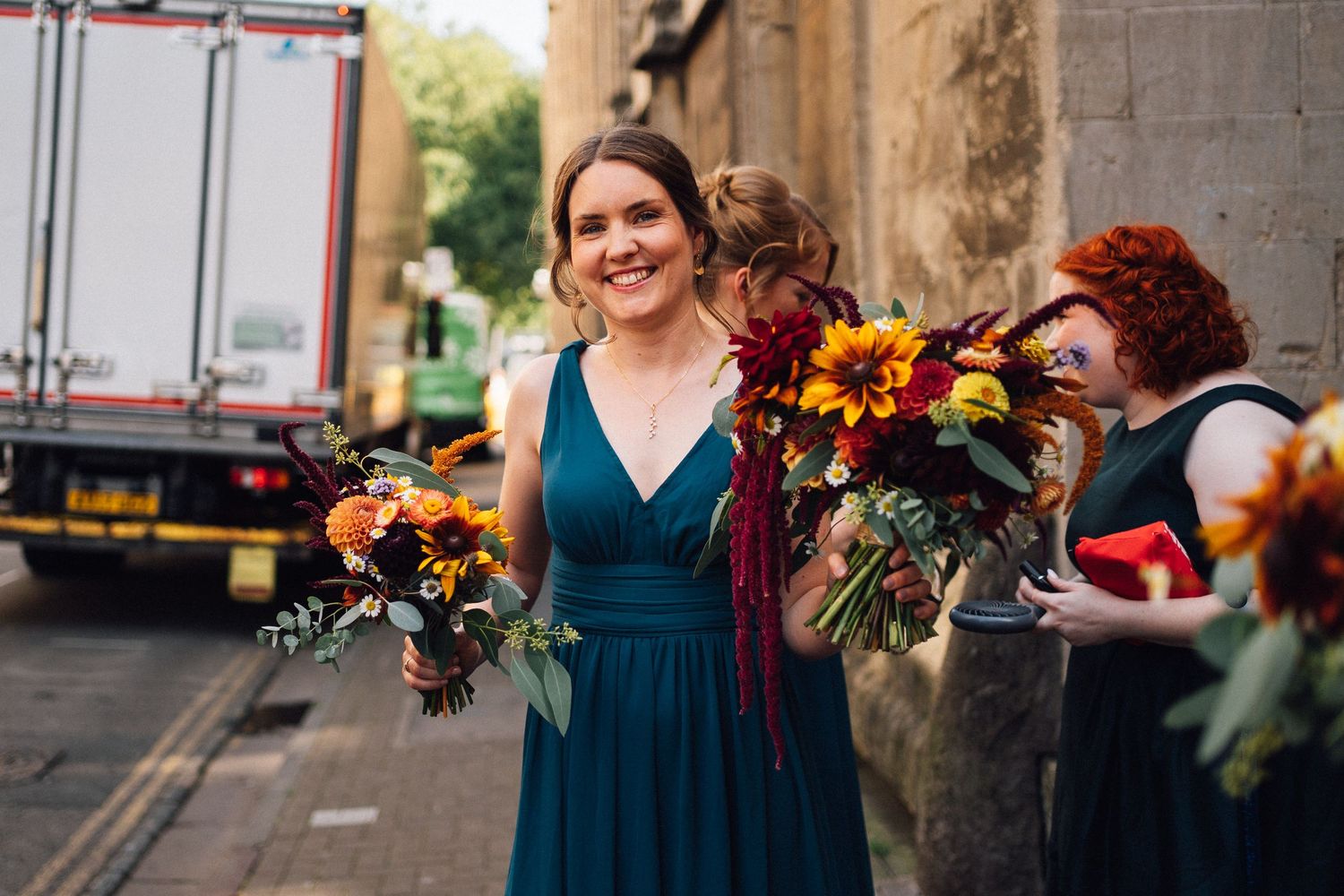 Woman in teal dress holding autumn-colored floral bouquet on city street.