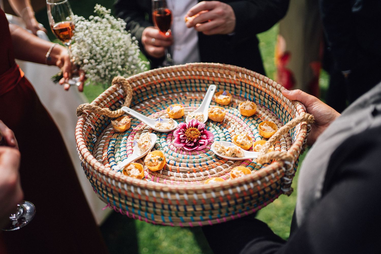 Appetizers and drinks being served on woven baskets during an outdoor wedding reception.