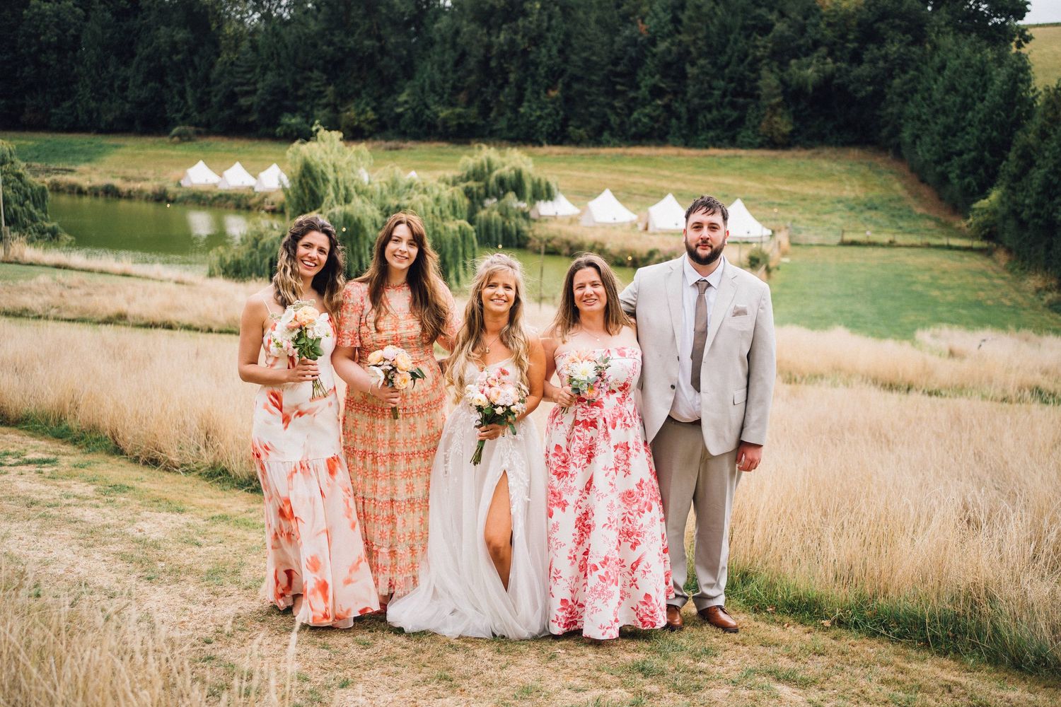 Wedding party posing in field with glamping tents visible in background.