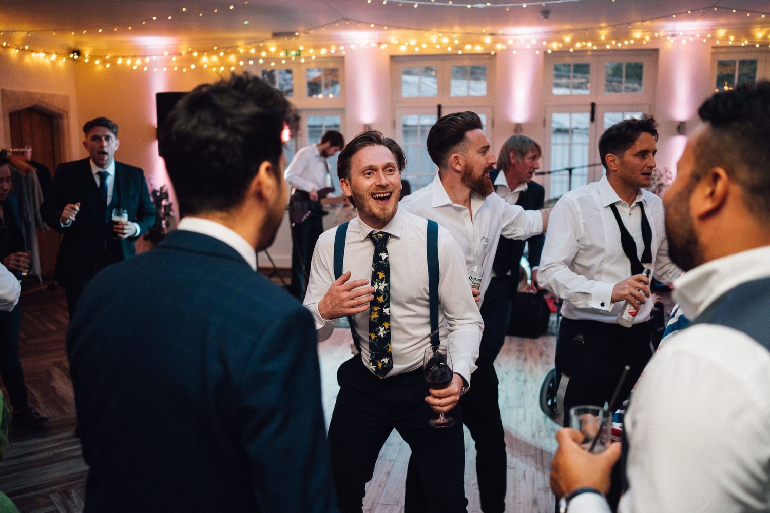 Wedding guests dancing and socializing at an evening reception with warm lighting.
