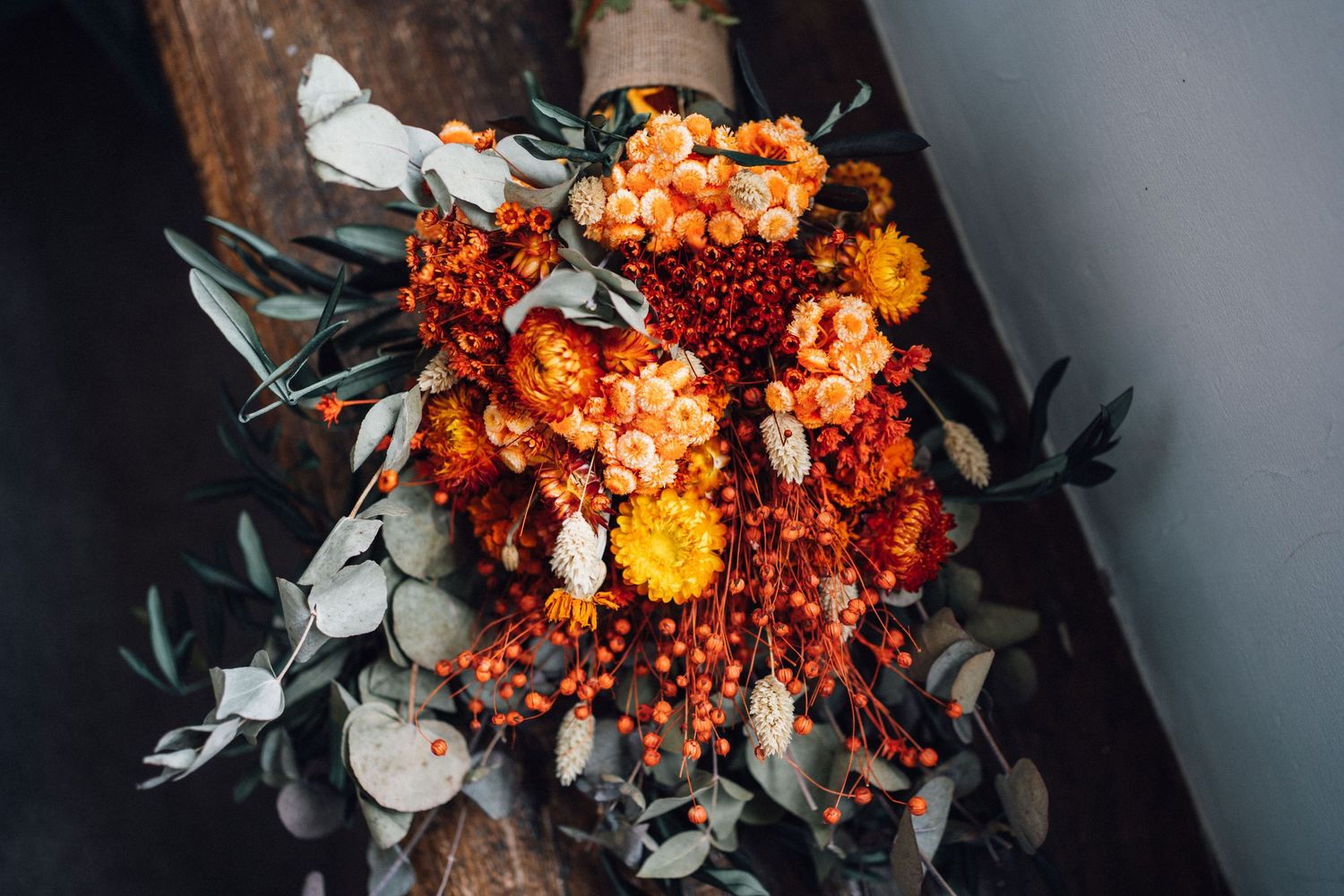 A stunning orange floral arrangement with marigolds and greenery against a dark moody background.
