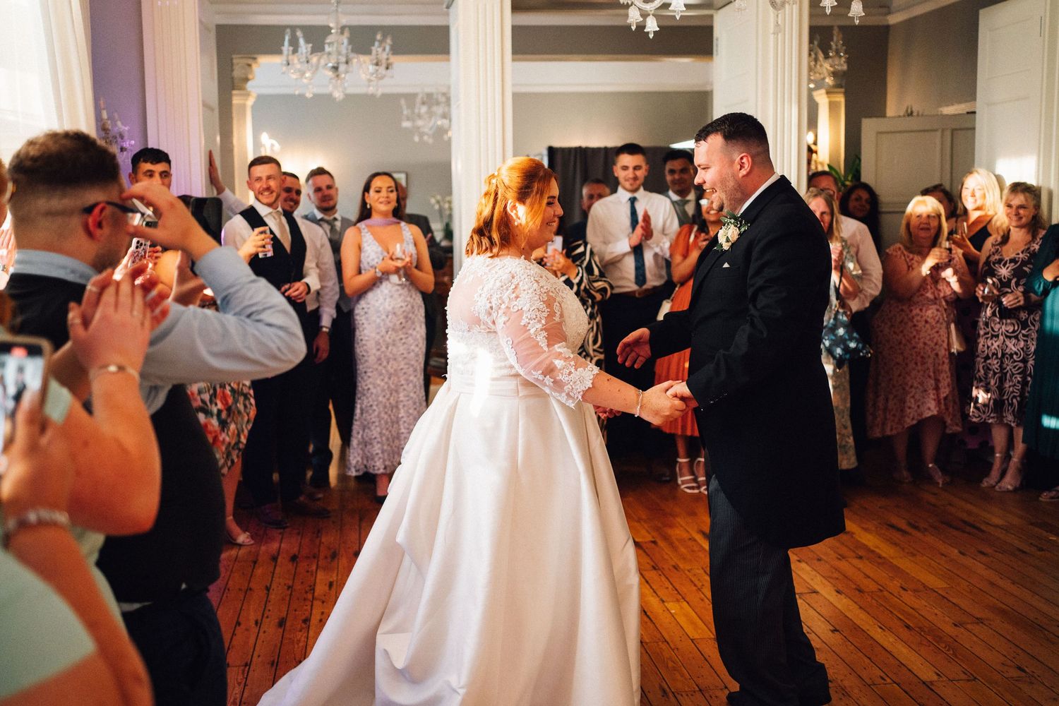 Wedding guests dancing and celebrating on a wooden dance floor at an indoor reception.
