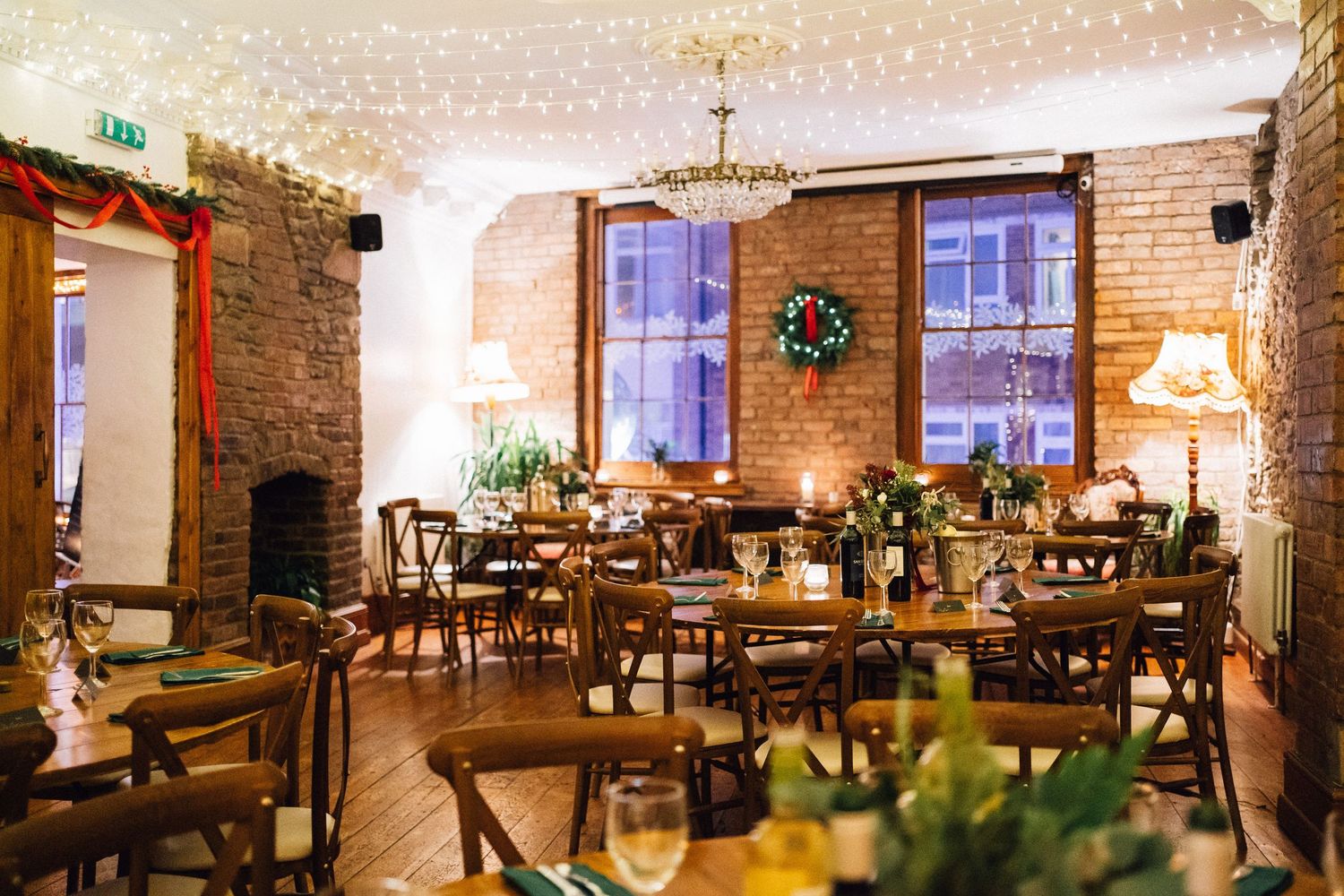 Cozy brick-walled restaurant interior with wooden tables and chairs under twinkling string lights.