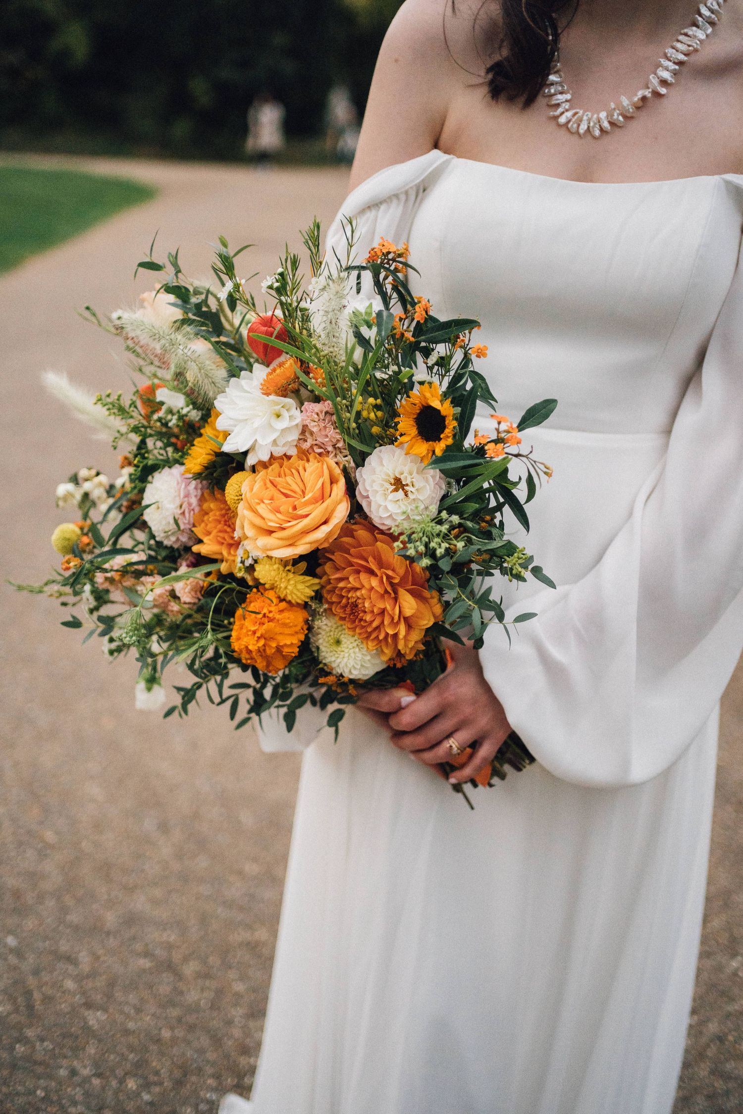 Elegant bridal bouquet featuring orange and white flowers with greenery against a flowing white dress.