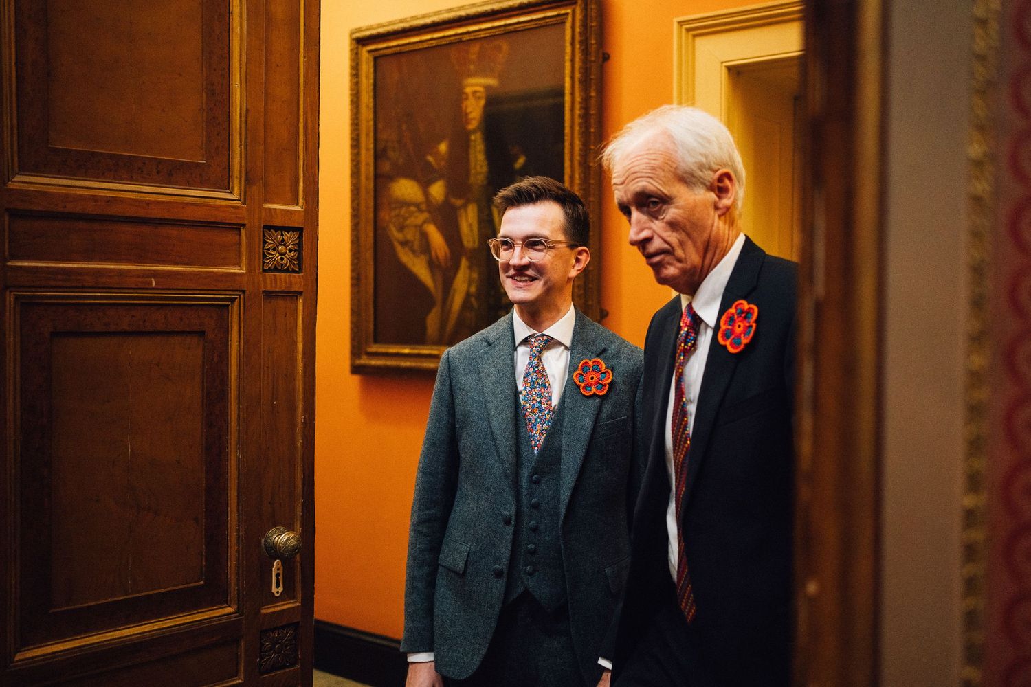 Group of officials in formal attire stand together during a ceremony in an ornate room with wood-paneled walls.