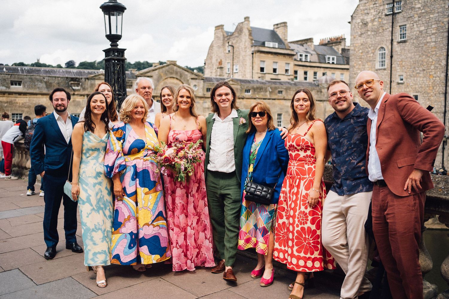 Group photo of wedding attendees standing together outside a historic stone building.