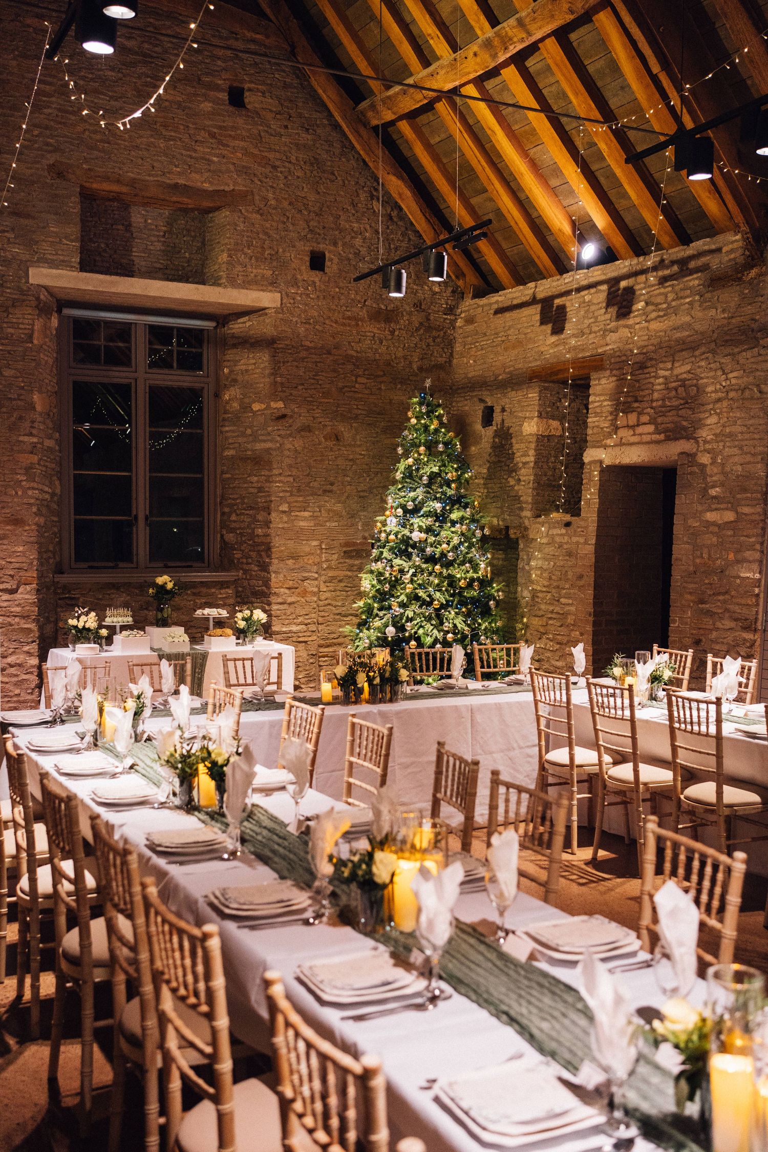 Rustic barn wedding reception setup with long tables, wooden chairs, and elegant floral centerpieces in a vaulted ceiling venue.