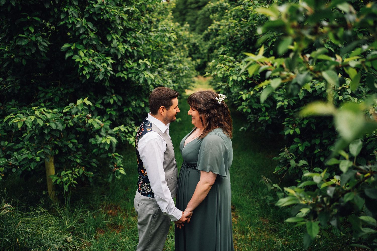 A couple shares romantic moments in a lush green garden setting during a wedding photoshoot.