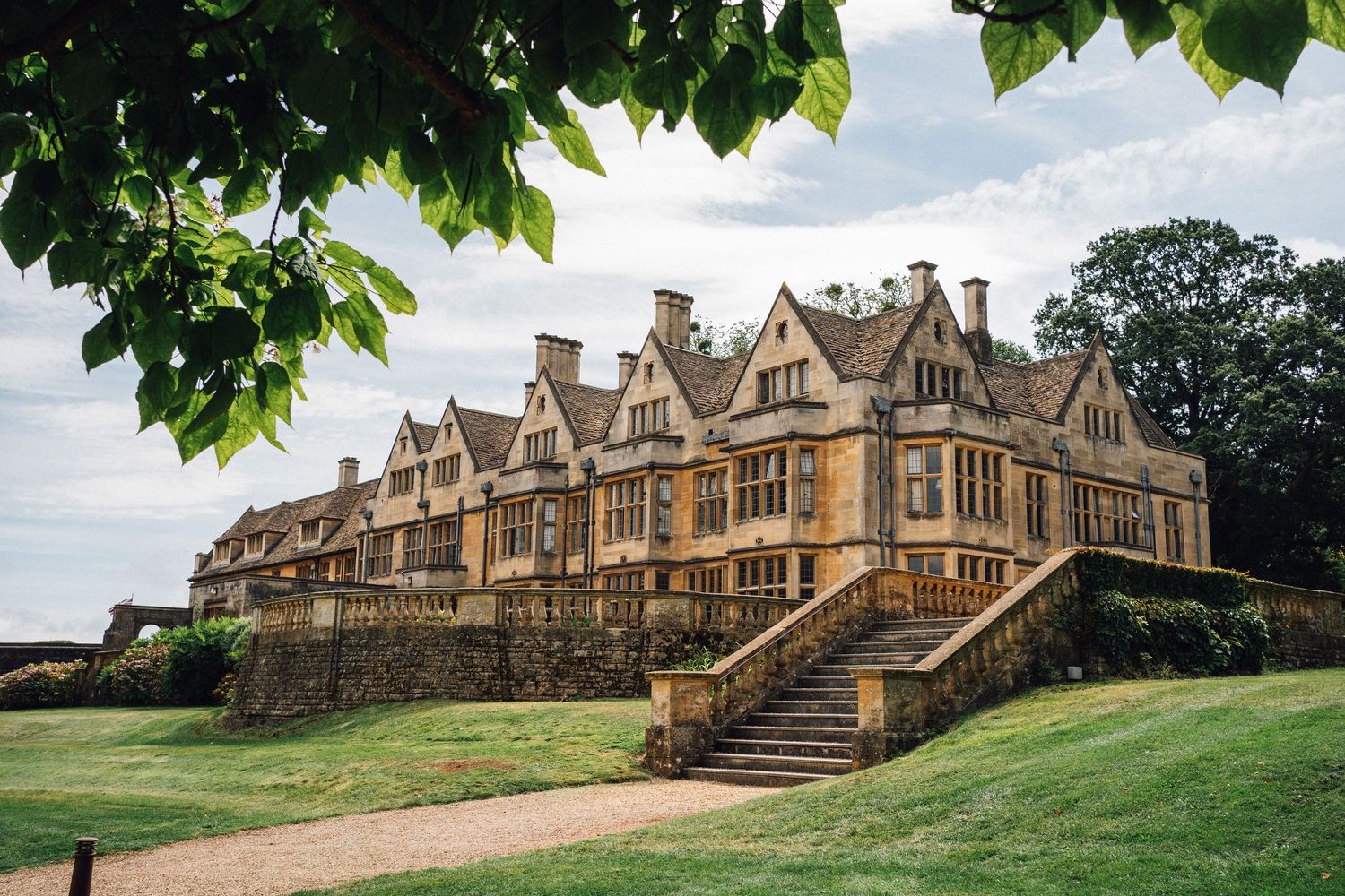 Panoramic view of a historic Cotswold stone manor house with gabled roofs and ornate architectural details in England.
