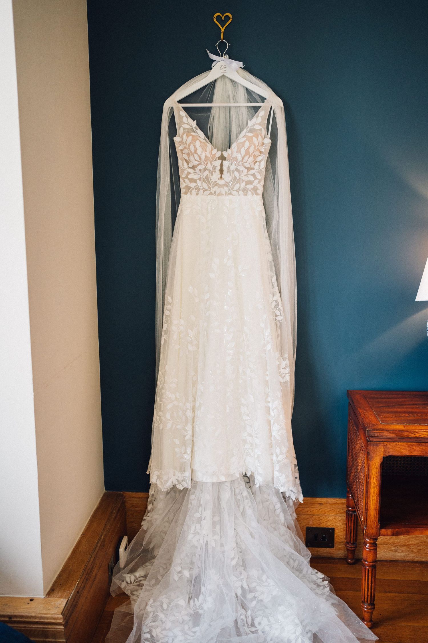 White lace wedding dresses displayed on hangers against a dark blue wall showing intricate details and designs.