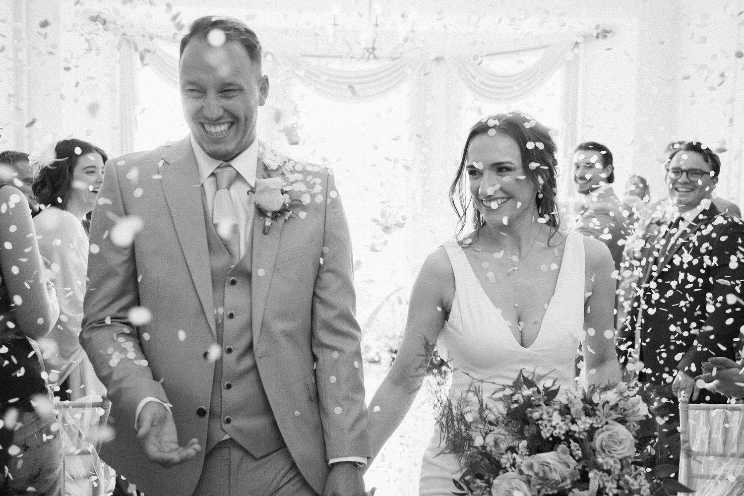 A joyful wedding celebration with confetti falling as guests celebrate in a bright outdoor setting.
