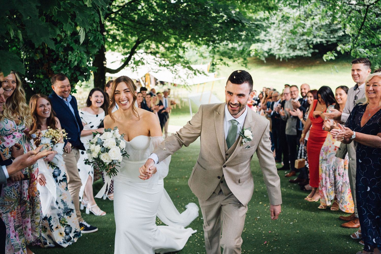 Wedding guests cheer and celebrate as newlyweds joyfully exit their outdoor garden ceremony.
