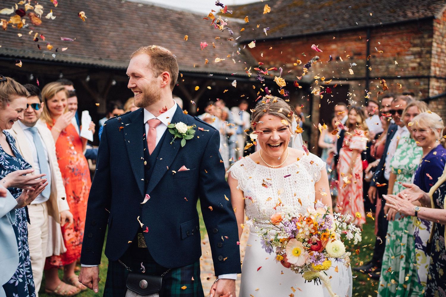 Joyful wedding celebration with confetti toss outside a rustic brick building.