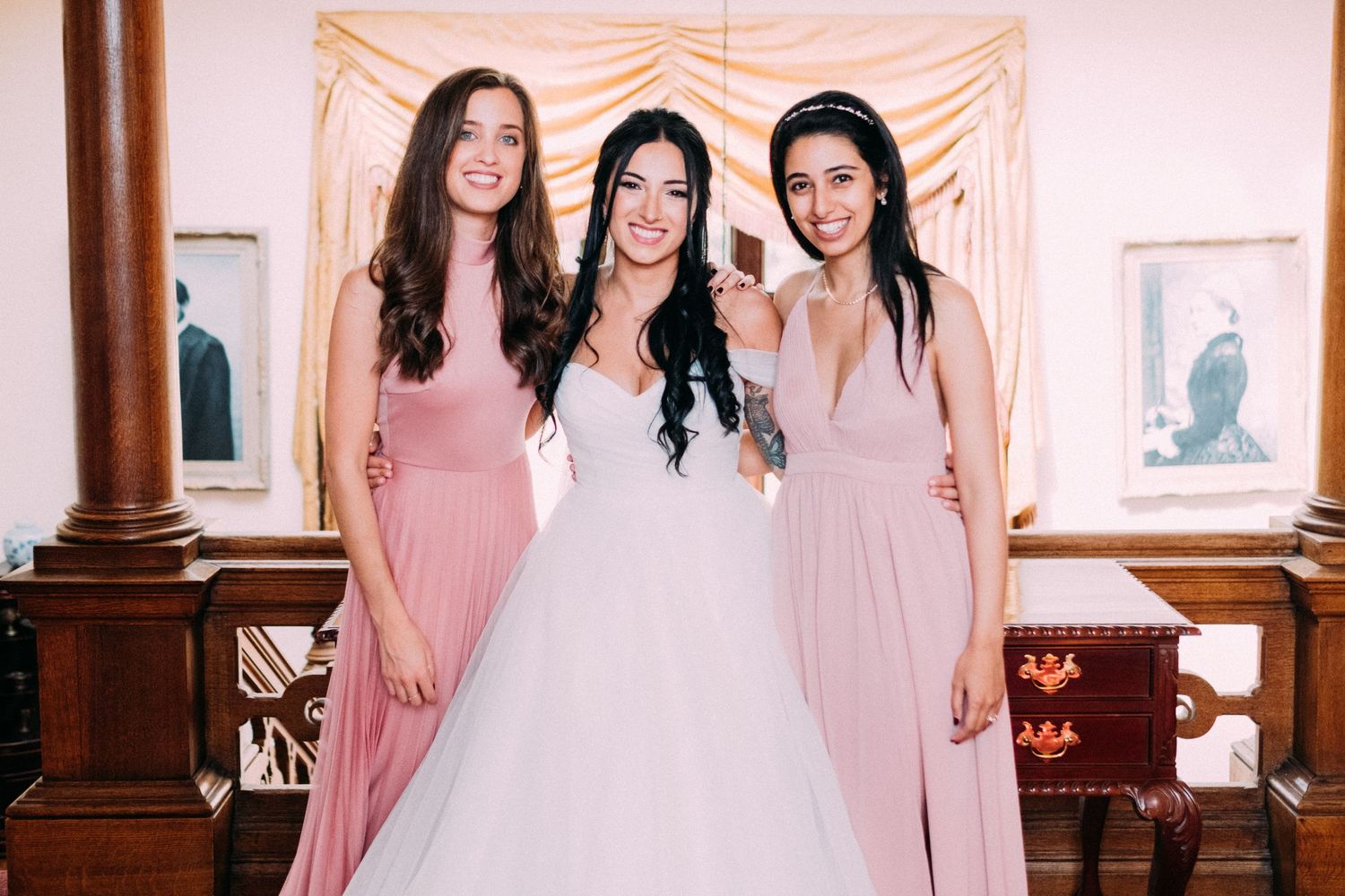 Bridesmaids in blush pink dresses pose together against a light backdrop.