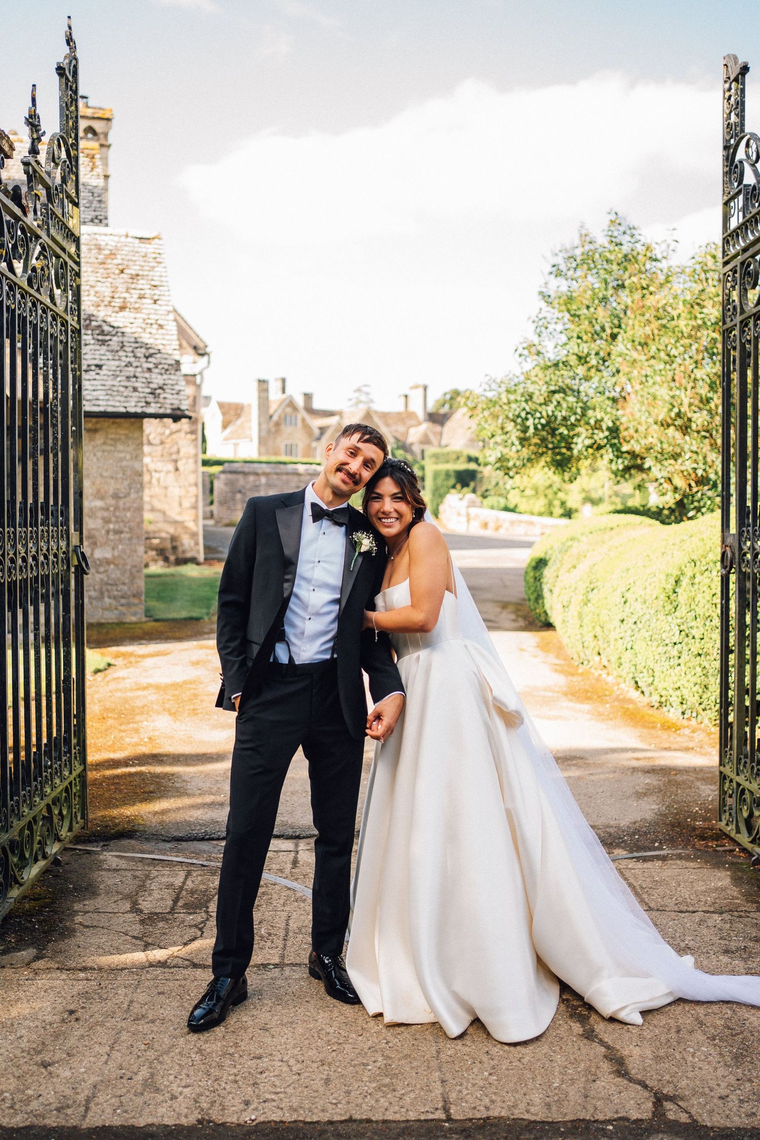 Elegant couple poses by ornate iron gates at their wedding venue.