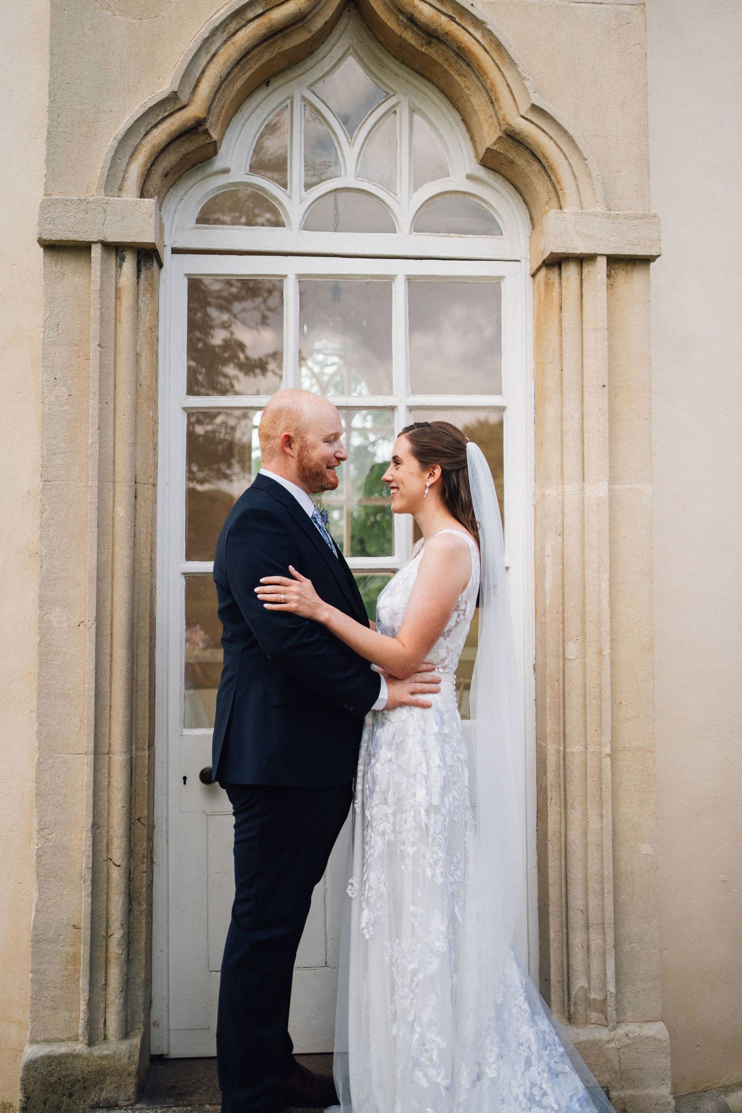 Bride and groom share a tender moment in front of elegant stone archways with white doors during their first look.