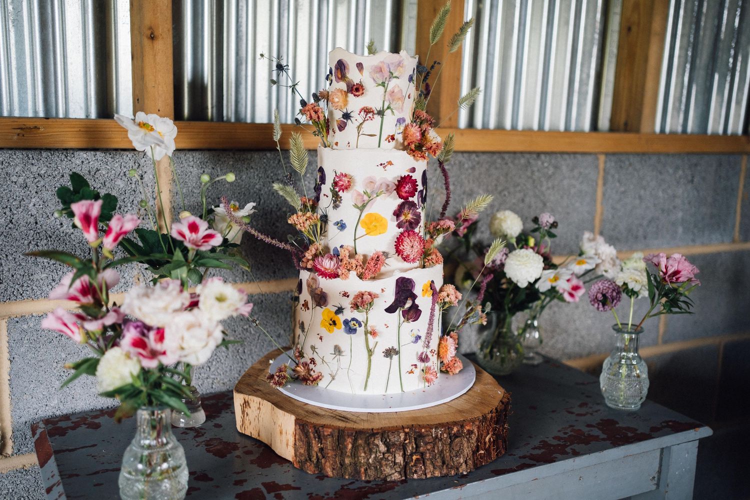 Elegant wedding cake display with floral decorations and rustic wood accents on a dark table setting.