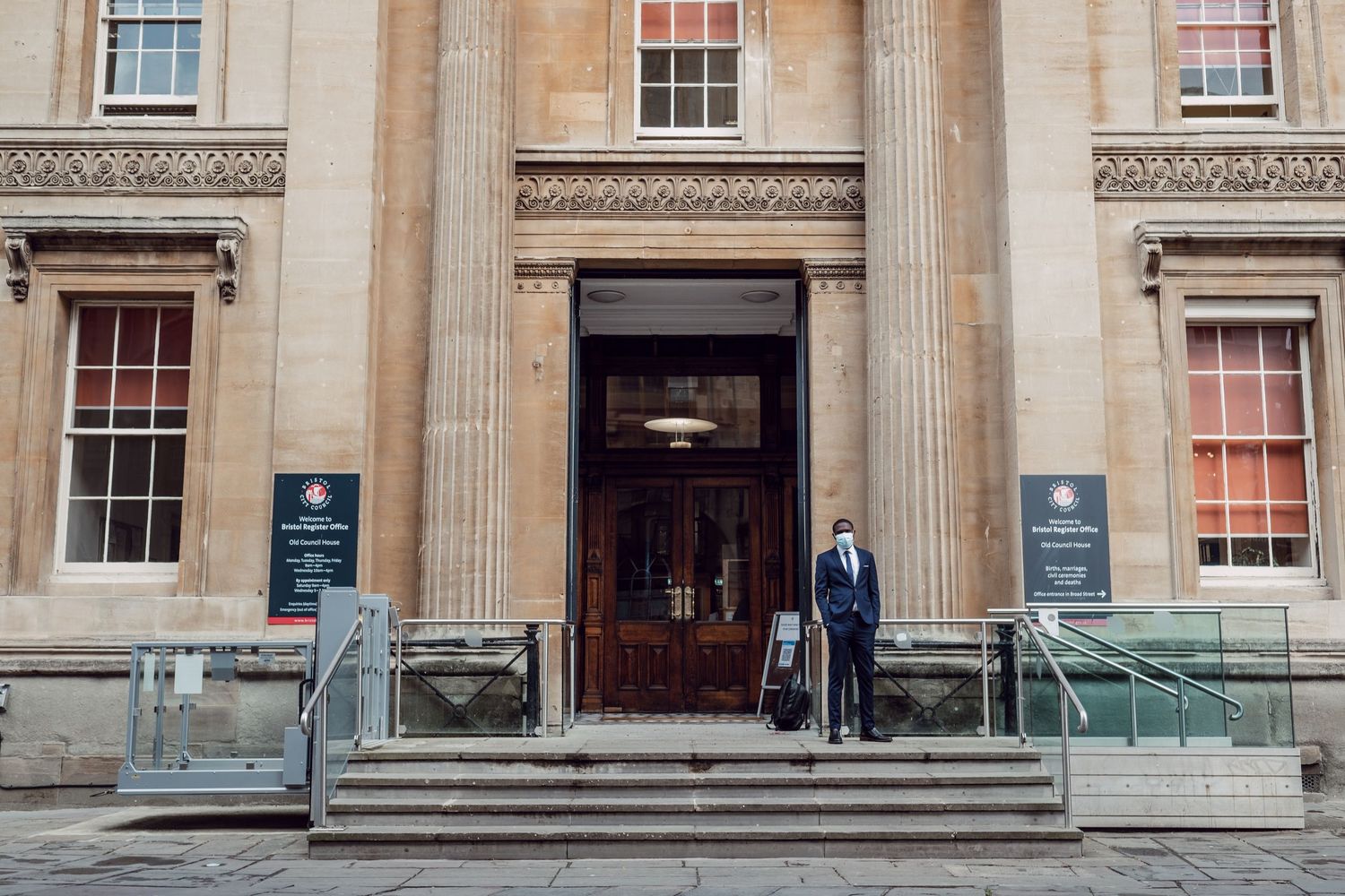 A grand stone building entrance with classical columns and steps leading to ornate wooden doors.