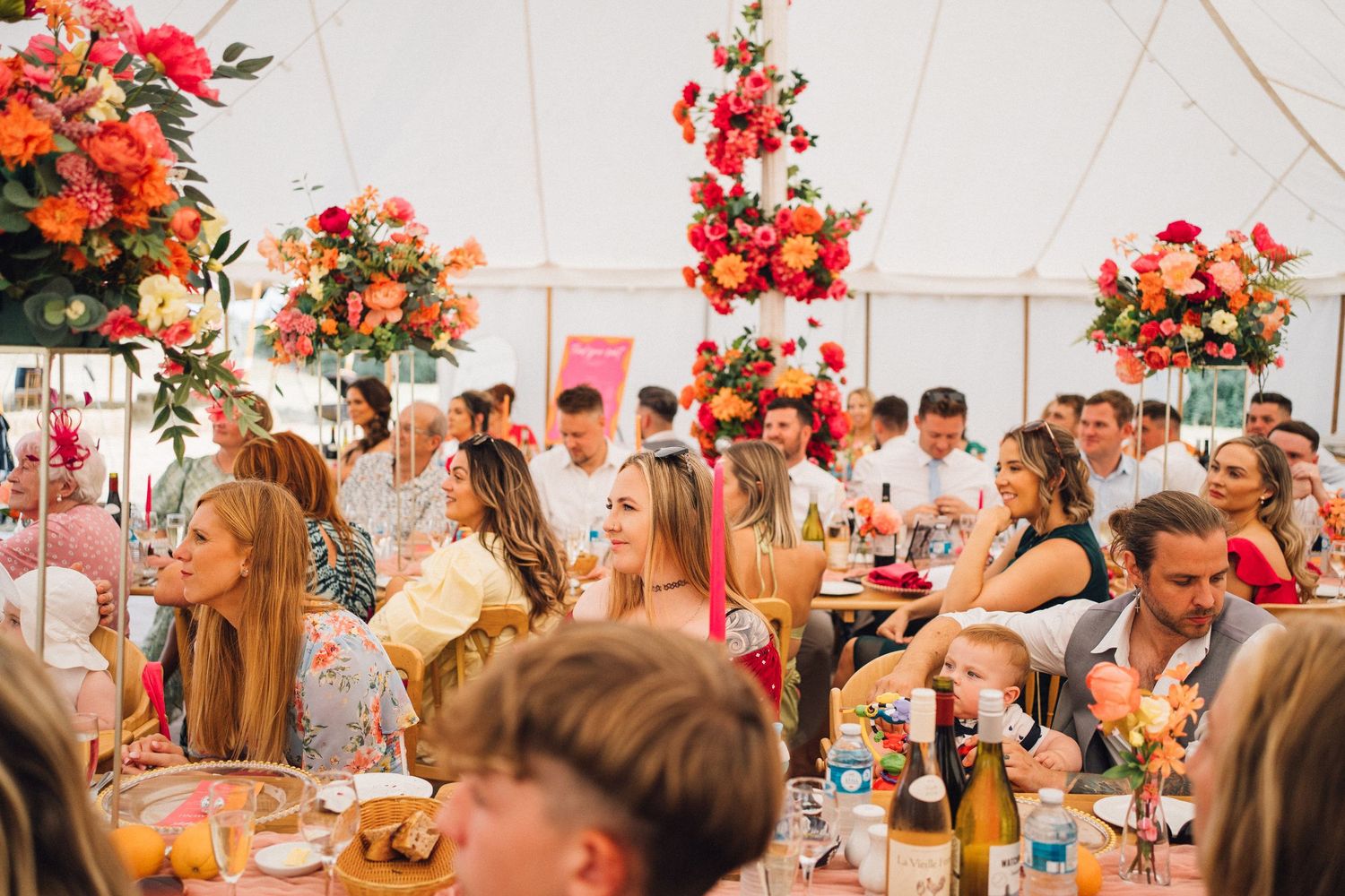 Wedding reception guests enjoy a vibrant coral-themed celebration under an elegant white tent with floral arrangements.