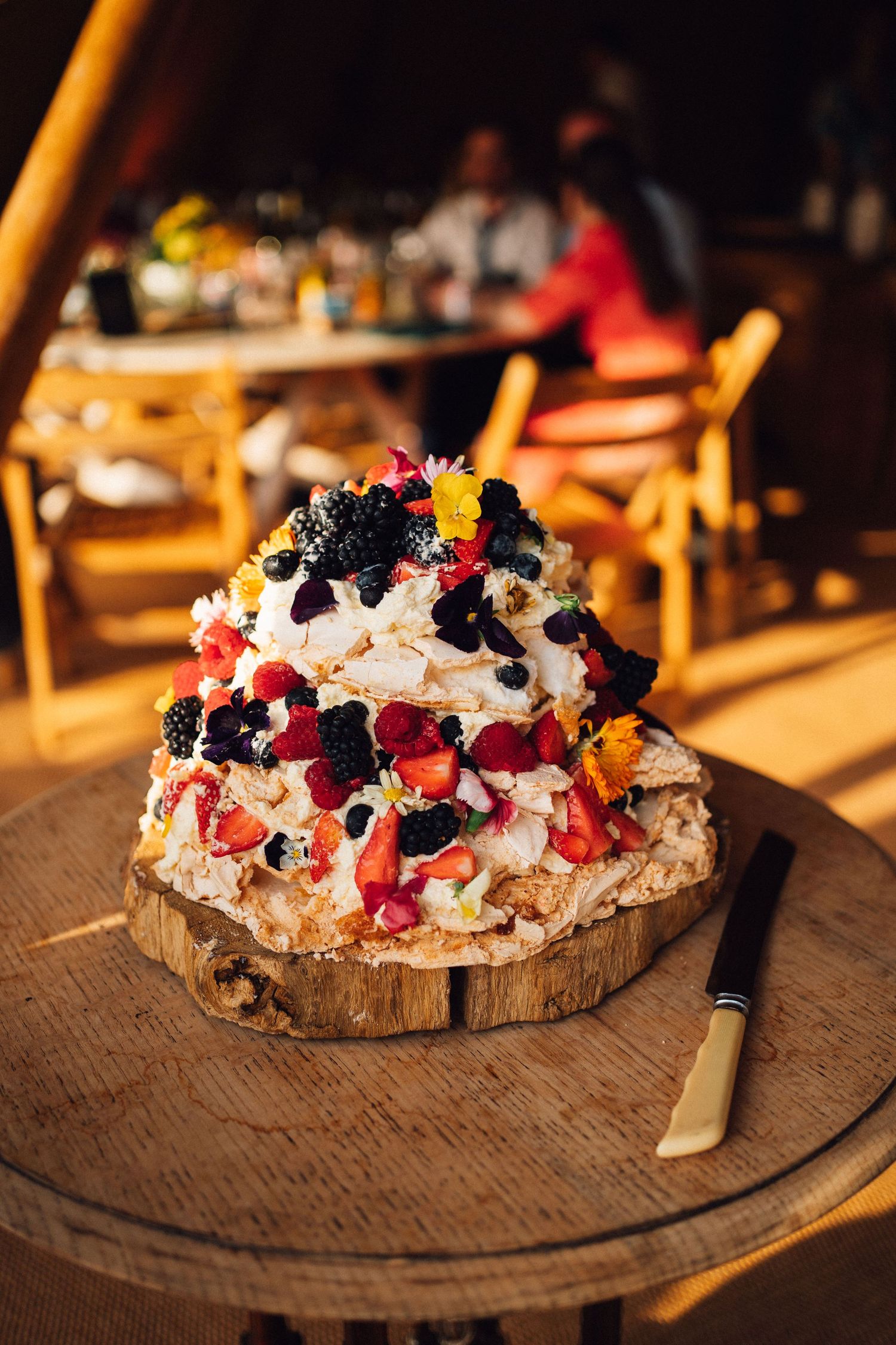 Rustic wooden board with creamy dessert topped with fresh berries, whipped cream and dark garnishes.