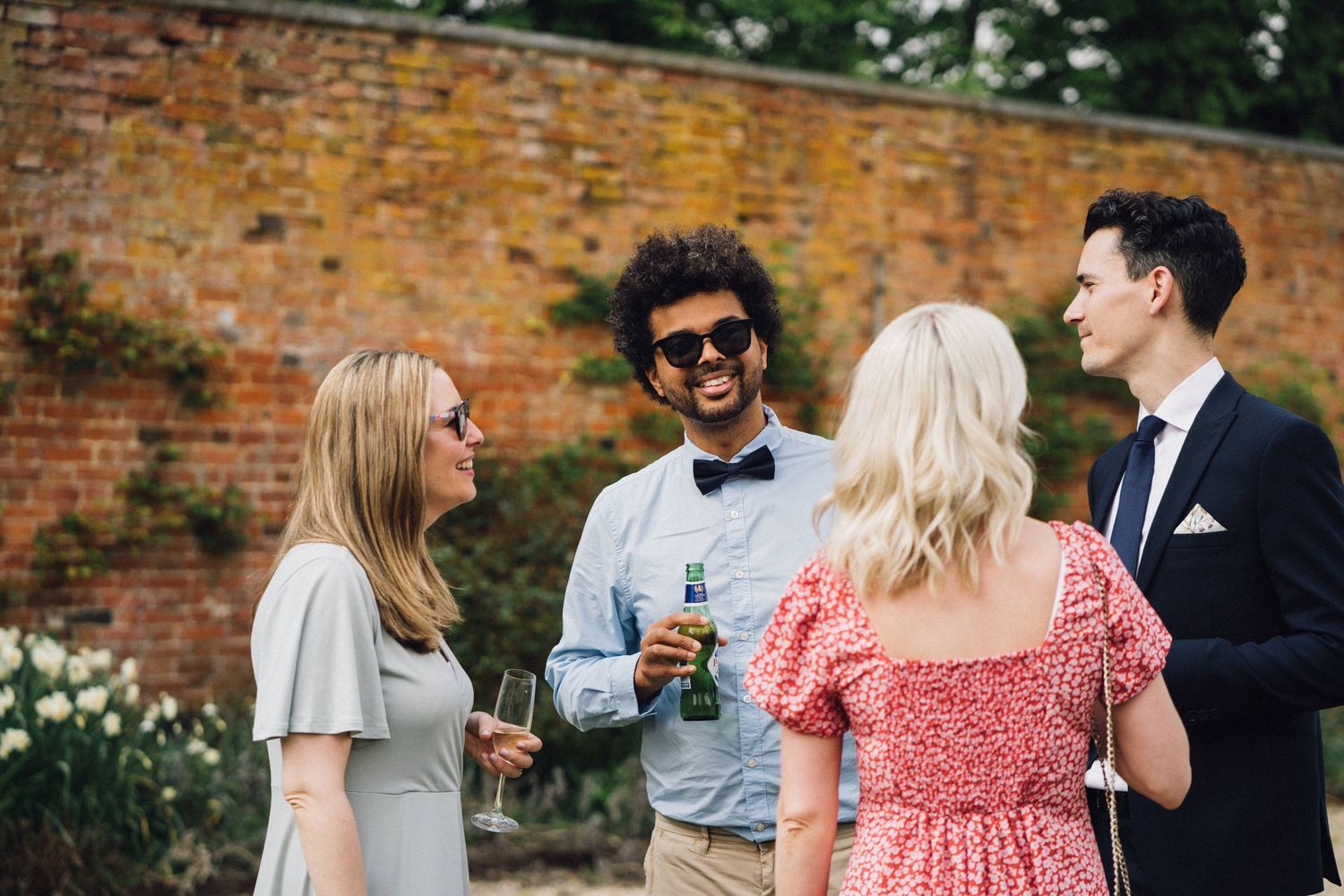Group of friends chatting and socializing at an outdoor garden party near a brick wall.