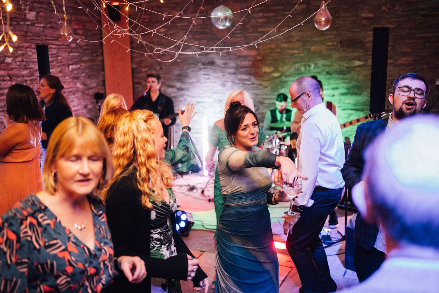 People dancing and celebrating at a nightclub or party venue with colorful lighting and brick walls.