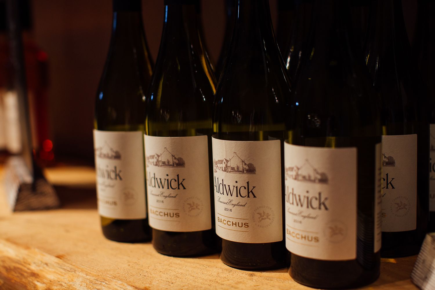 Rows of Chadwick Bacchus white wine bottles displayed on a wooden surface in warm ambient lighting.