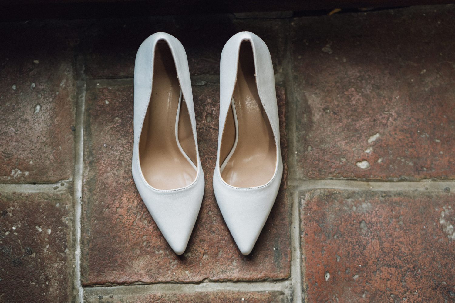 Elegant white bridal shoes displayed against a rustic brick wall background.