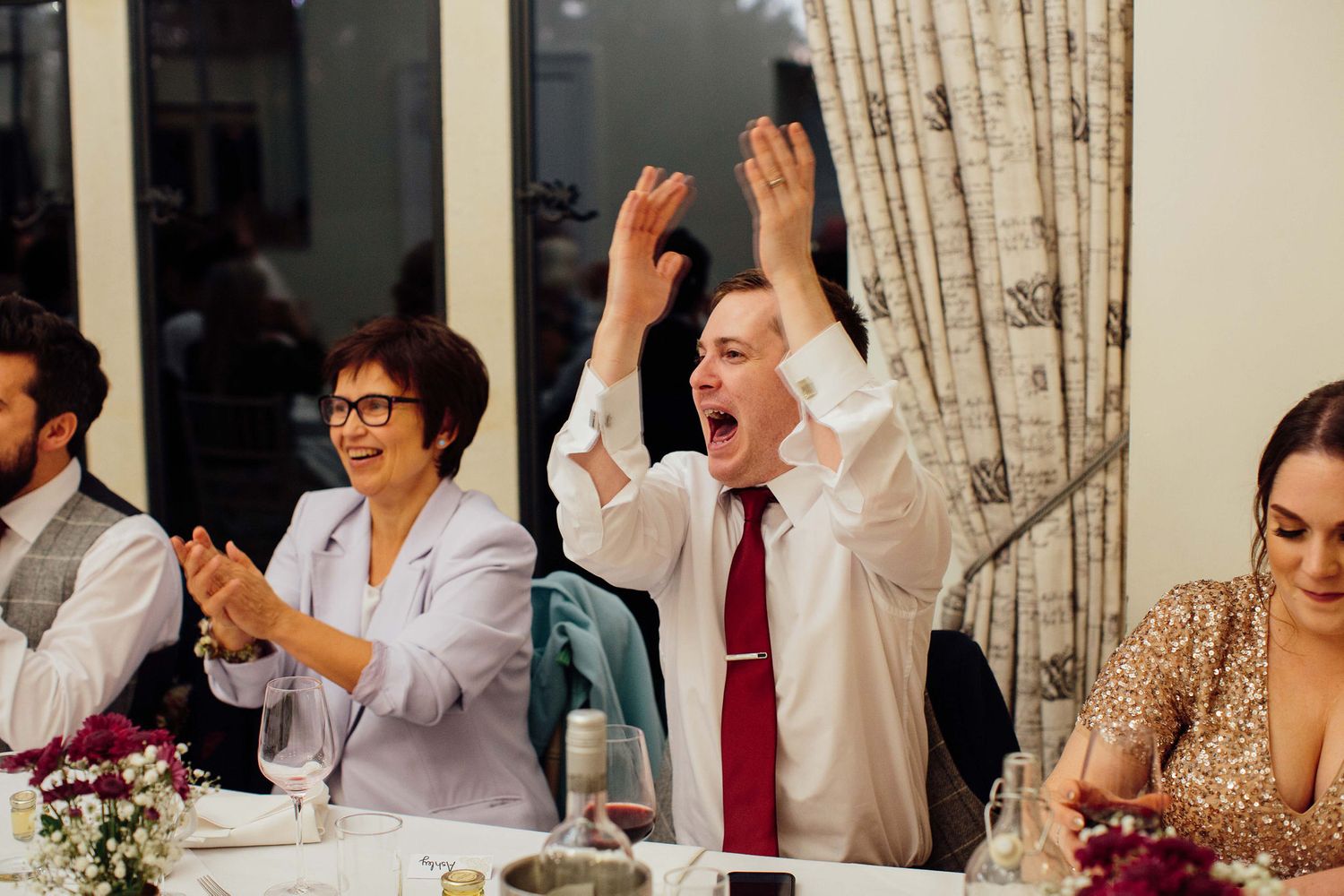 Wedding reception guests raising hands in celebration at elegant indoor venue.