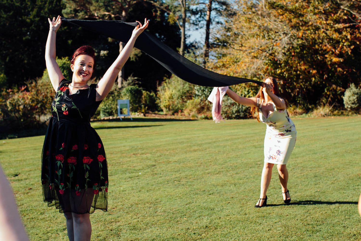 Wedding guests enjoying themselves on a sunny lawn with autumn trees in the background.