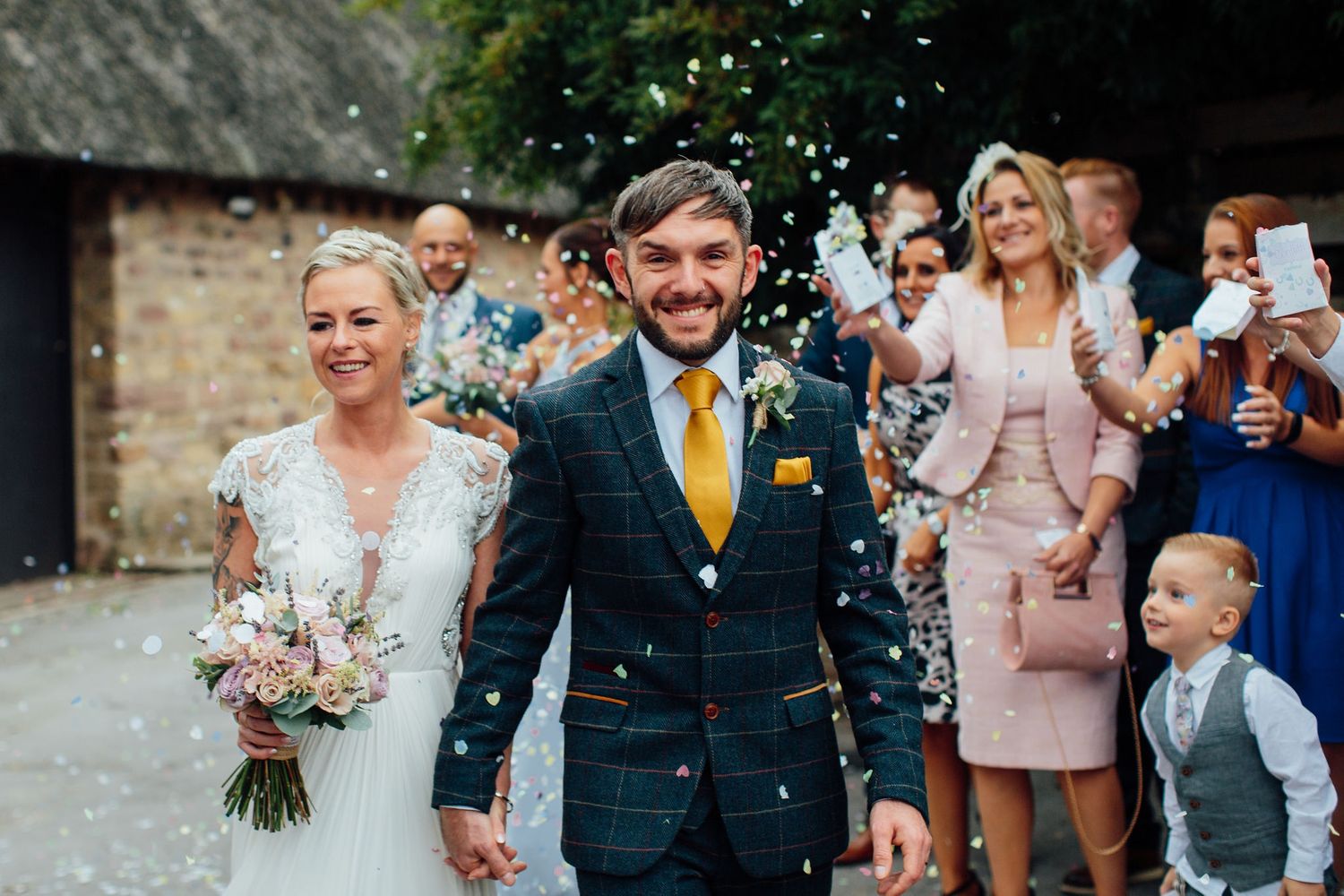 Wedding celebration with confetti and guests cheering for the newlyweds outside a brick building.