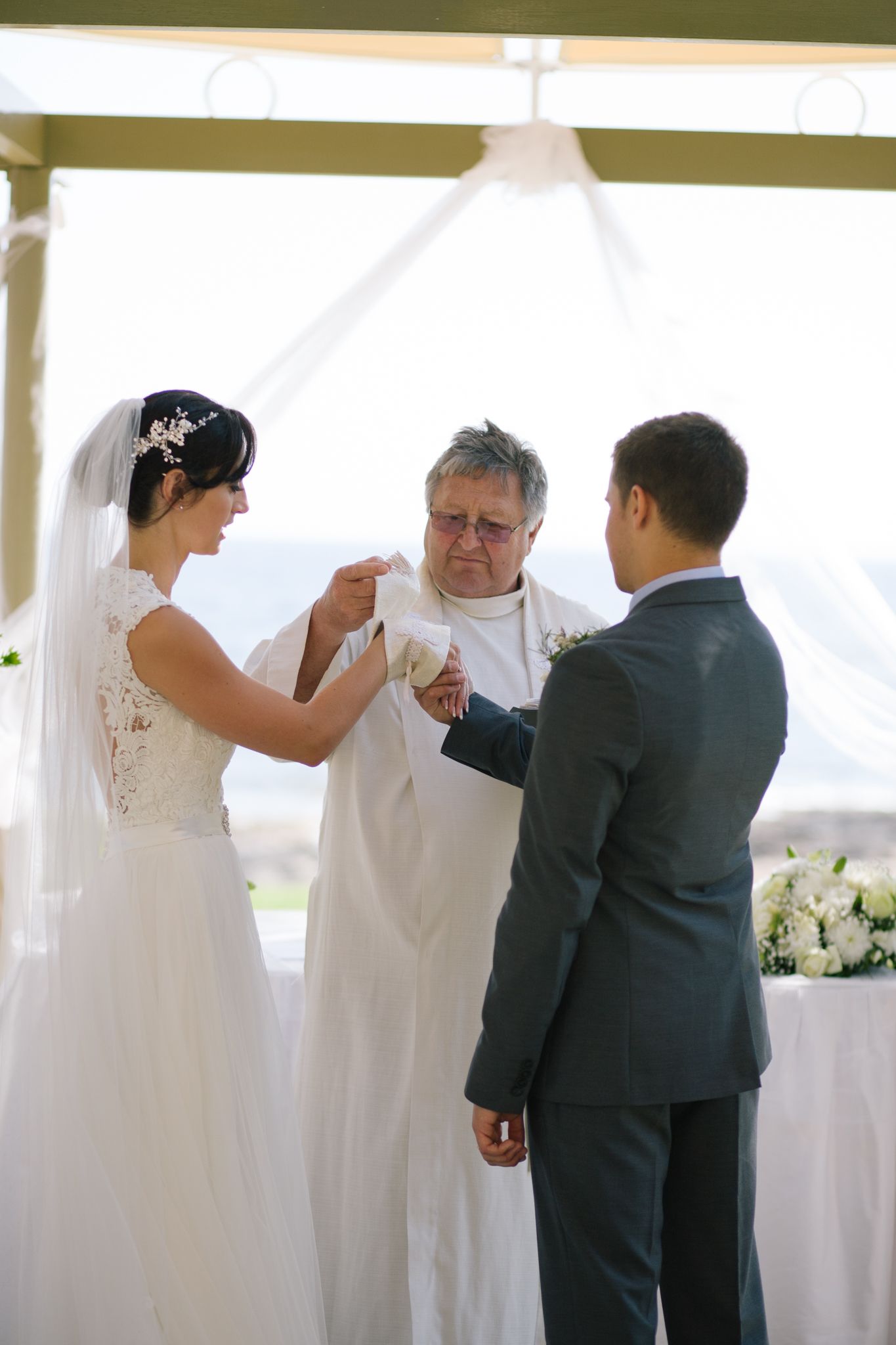 Wedding ceremony candid moments under white tent with floral arrangements.