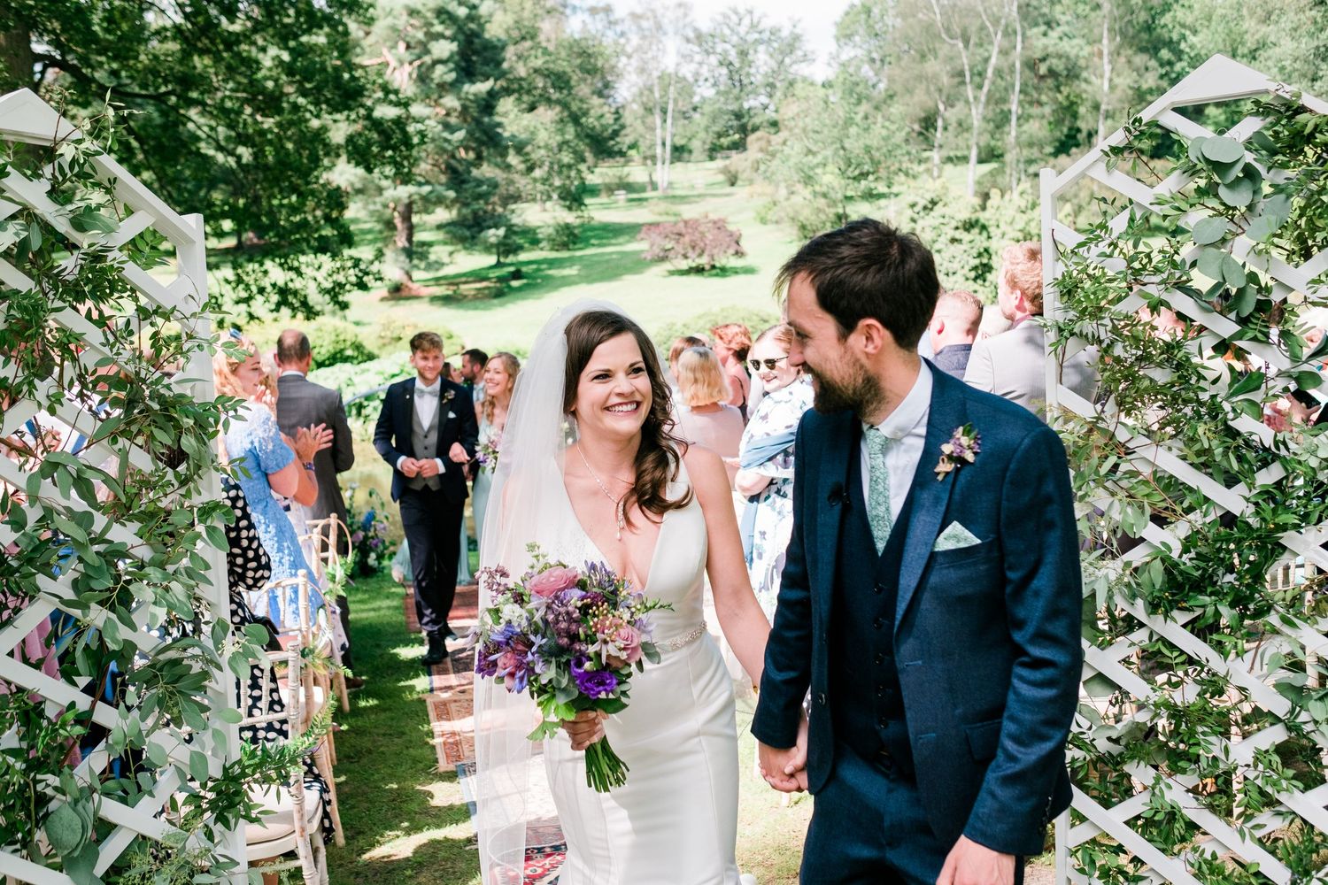 Elegant outdoor wedding ceremony in a garden setting with flowering trees and guests.