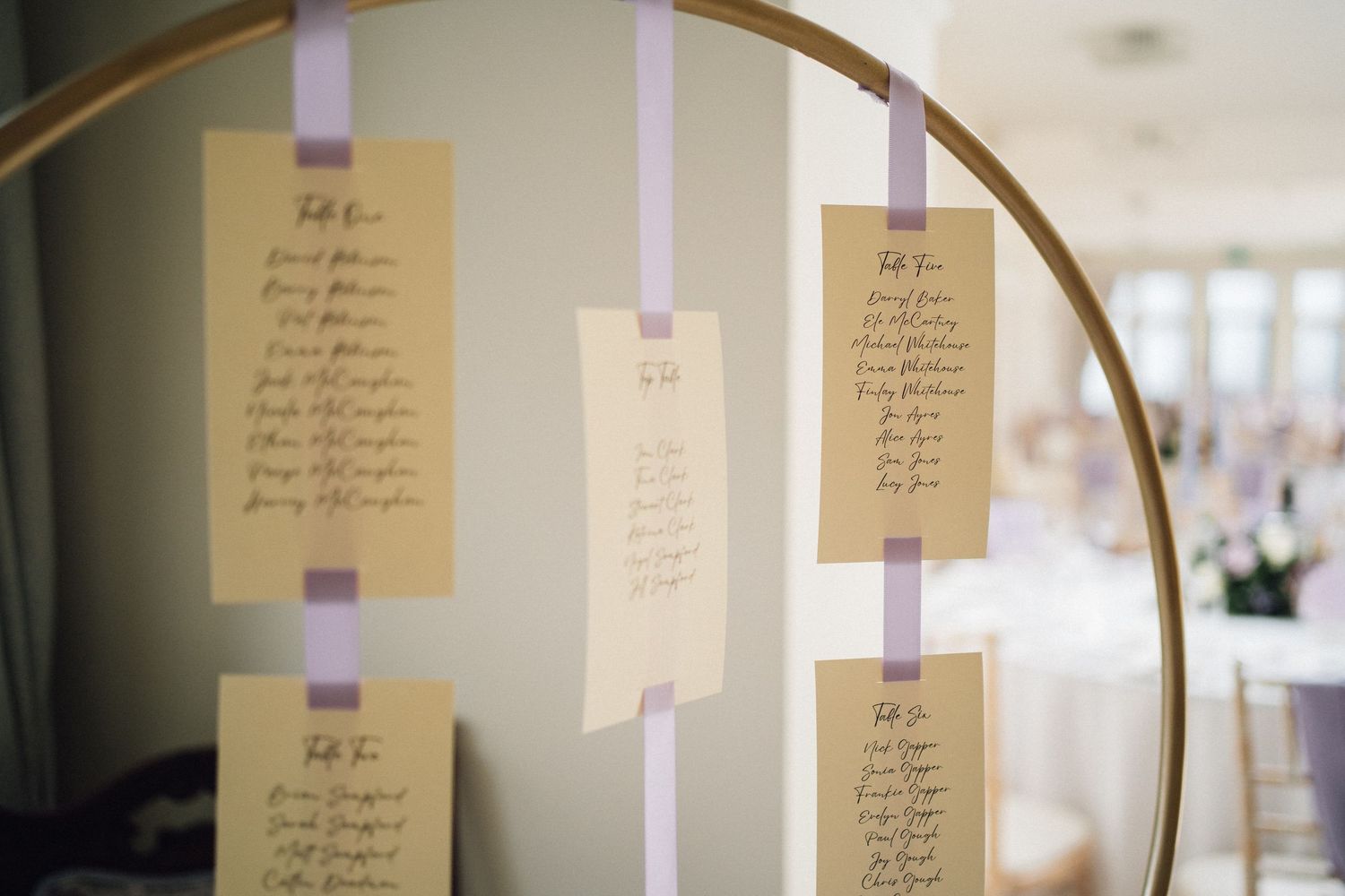 Handwritten wedding escort cards hanging on delicate ribbons from a curved gold arch display.
