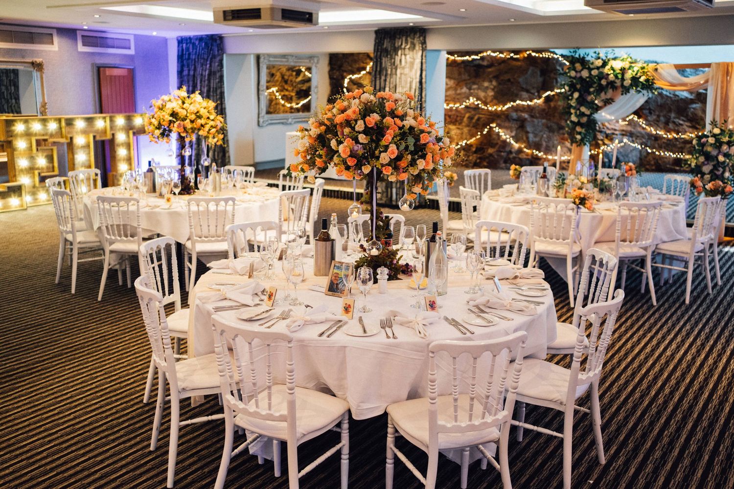 Elegant wedding reception venue with white table settings and floral centerpieces under ambient lighting.