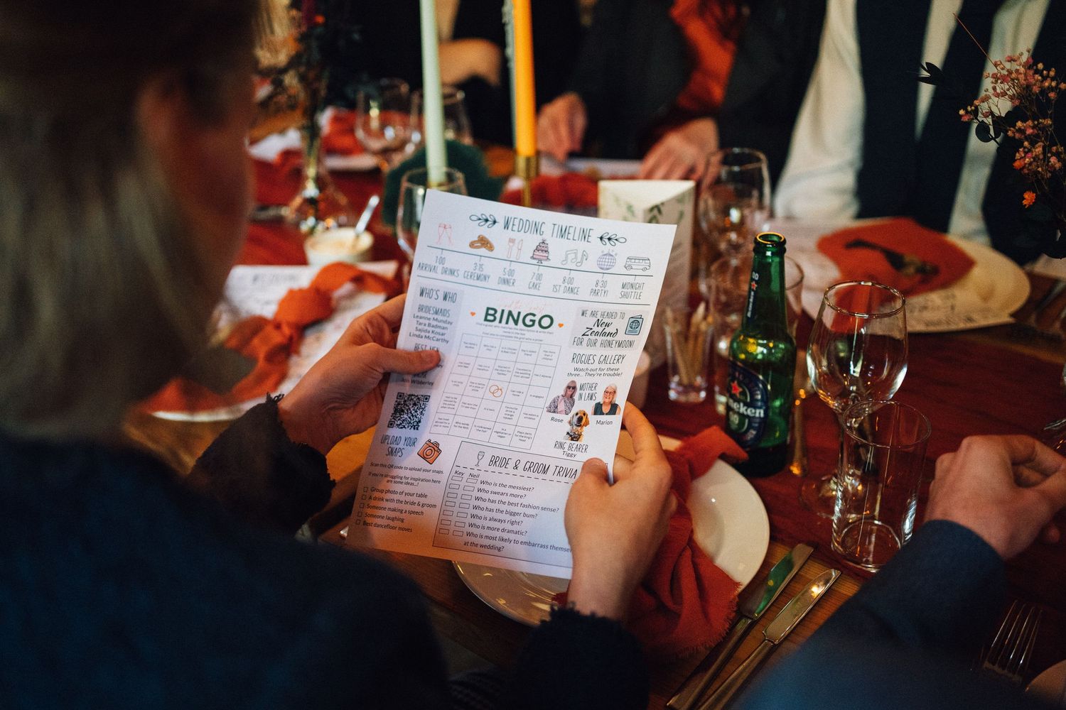 A group of people playing bingo at a table with drinks and cards visible in a dimly lit setting.